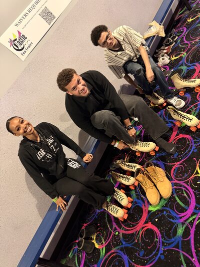 Three team members lacing up roller skates at the rink